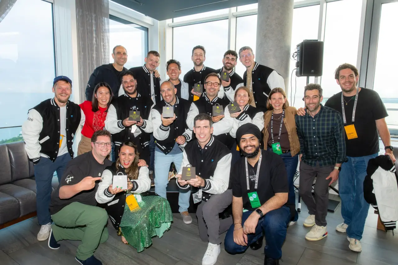 A large group of 2026 Shopify Build Award winners posing together indoors, wearing matching varsity jackets and holding their individual award bags.