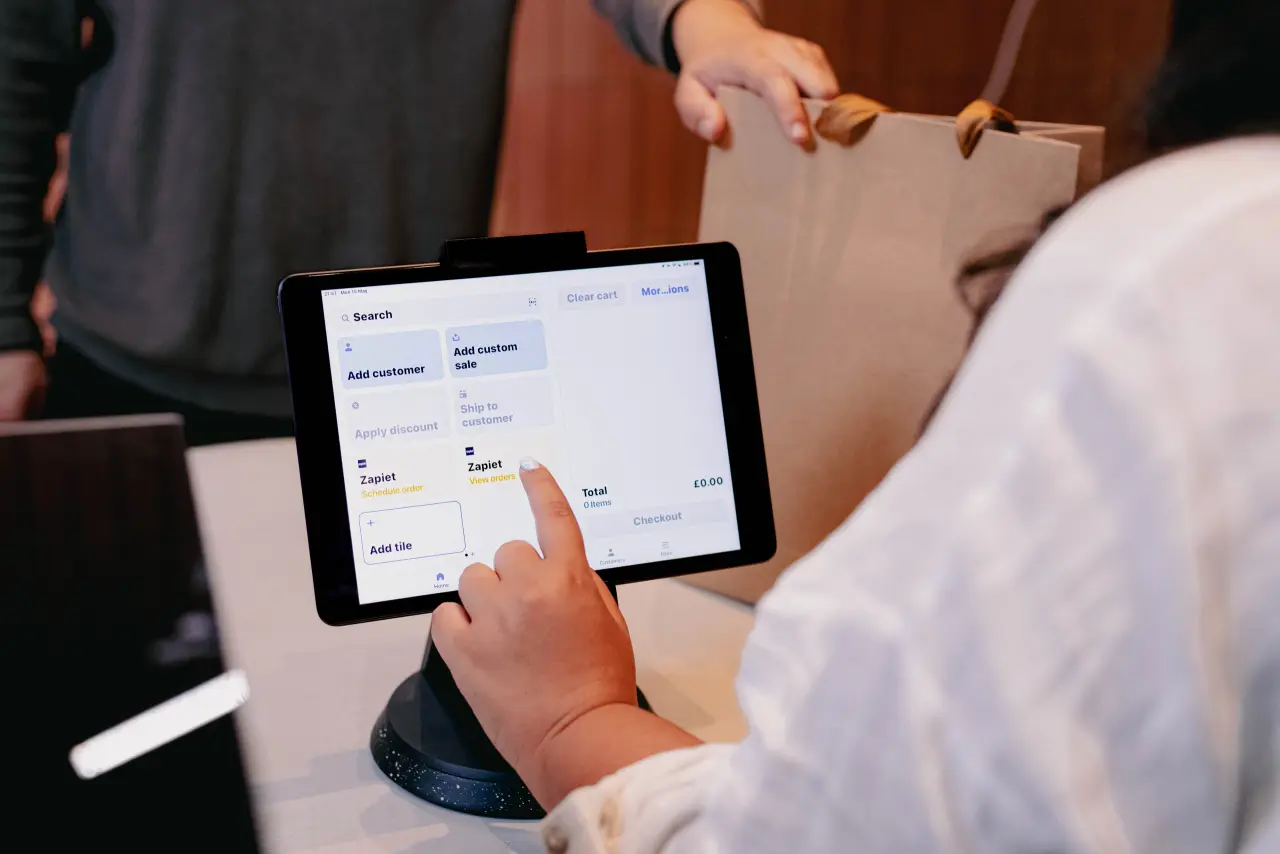 Shop assistant tapping the Zapiet View orders tile in Shopify POS while a customer collects their order