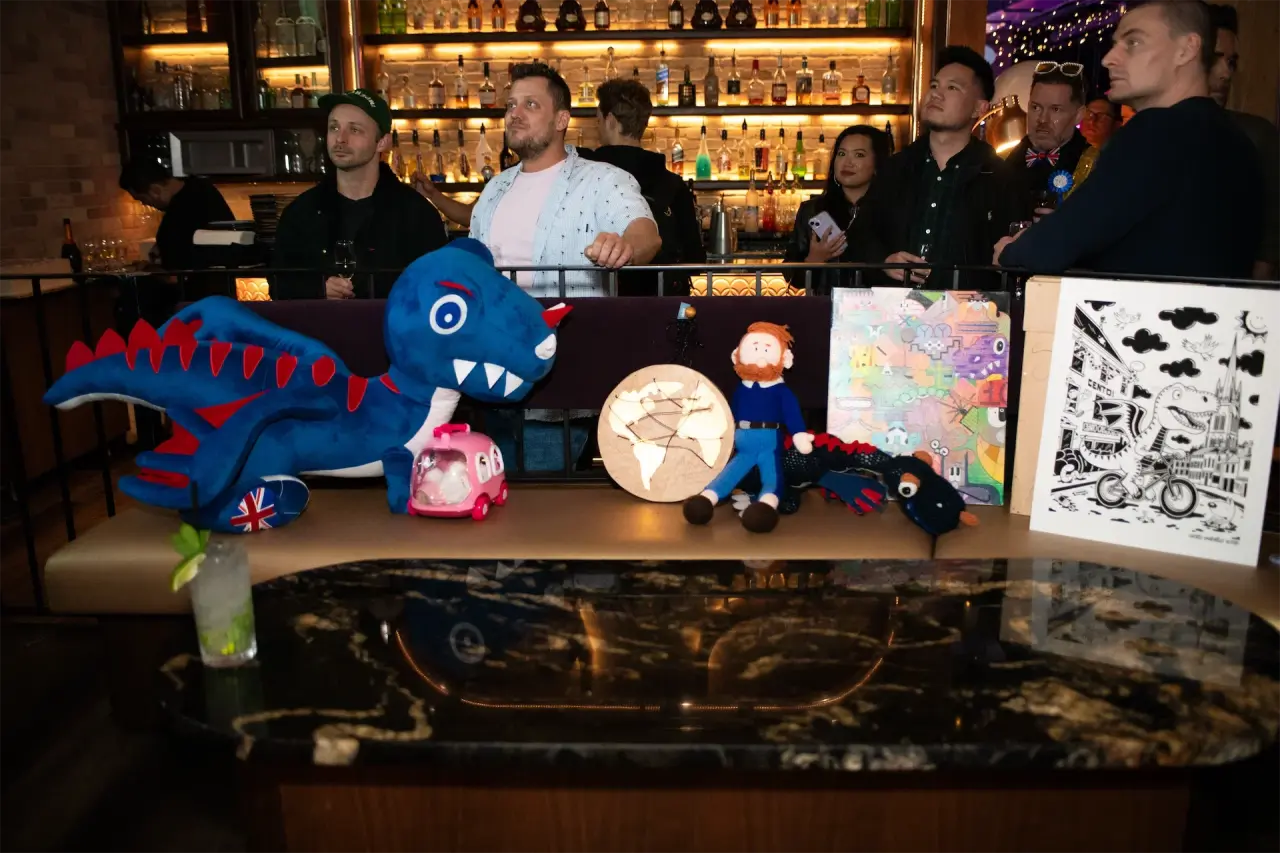 Zapietousaurus plush toy next to embroidered globe artwork and a black-and-white illustrated piece, displayed on a bar at the Epic Party.