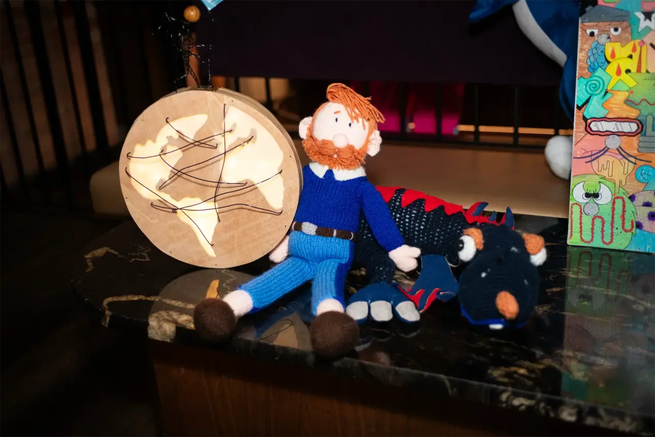 Hand-knitted figures including a person and the Zapietousaurus mascot, displayed alongside the artwork by Patrícia Serafim.